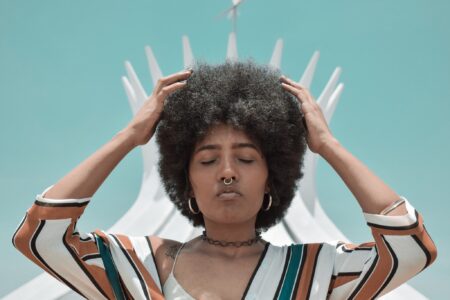 Woman touching her afro with her eyes closed against a blue sky.