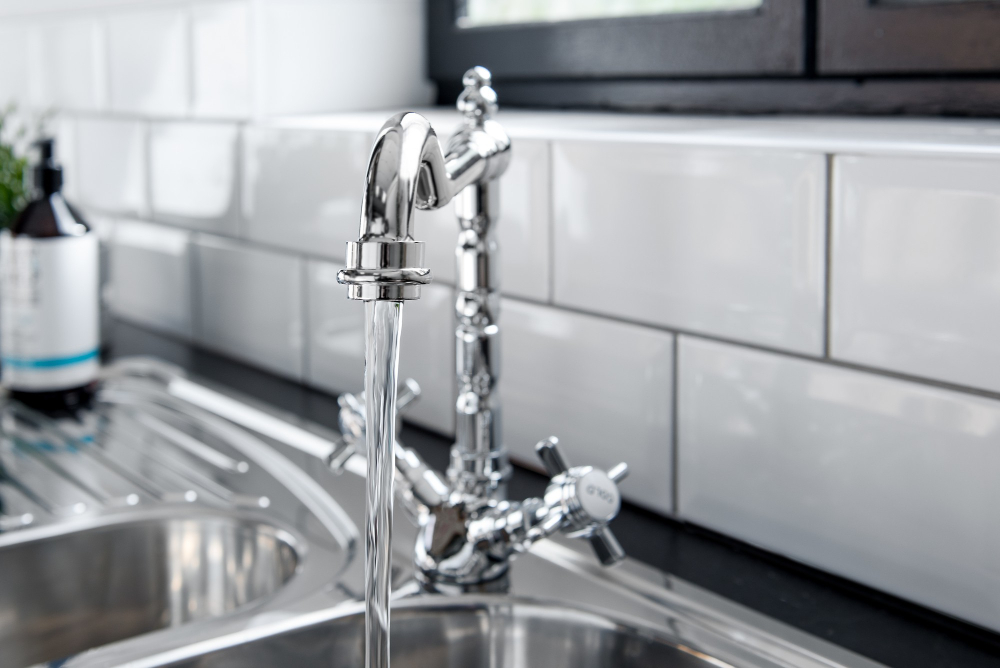 A faucet in a kitchen against subway tile with running water