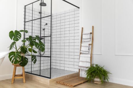 Bathroom shower with subway tile surrounded by plants and towel rack